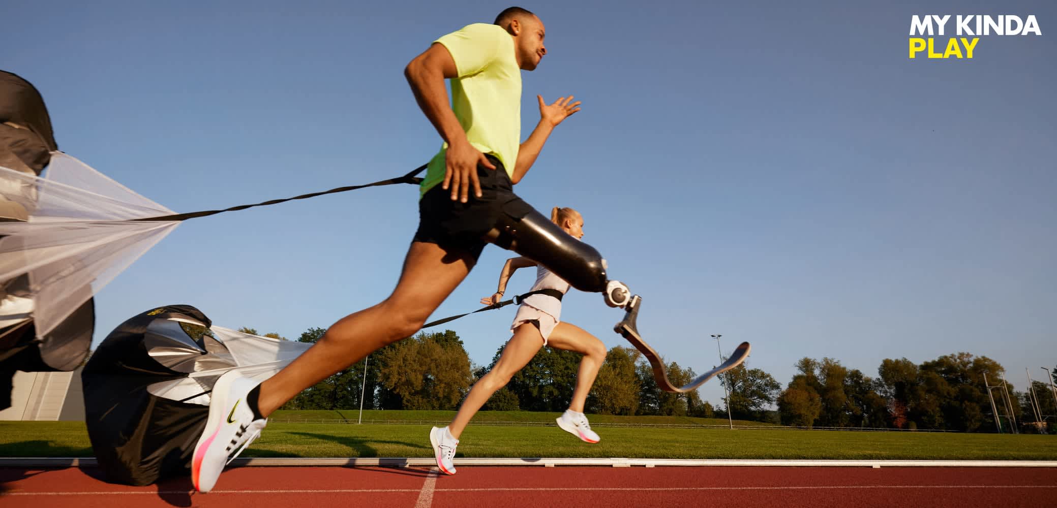 Two athletes running on a track. One wears a green shirt and black shorts, with a running blade. The other in a white top and shorts, also running.